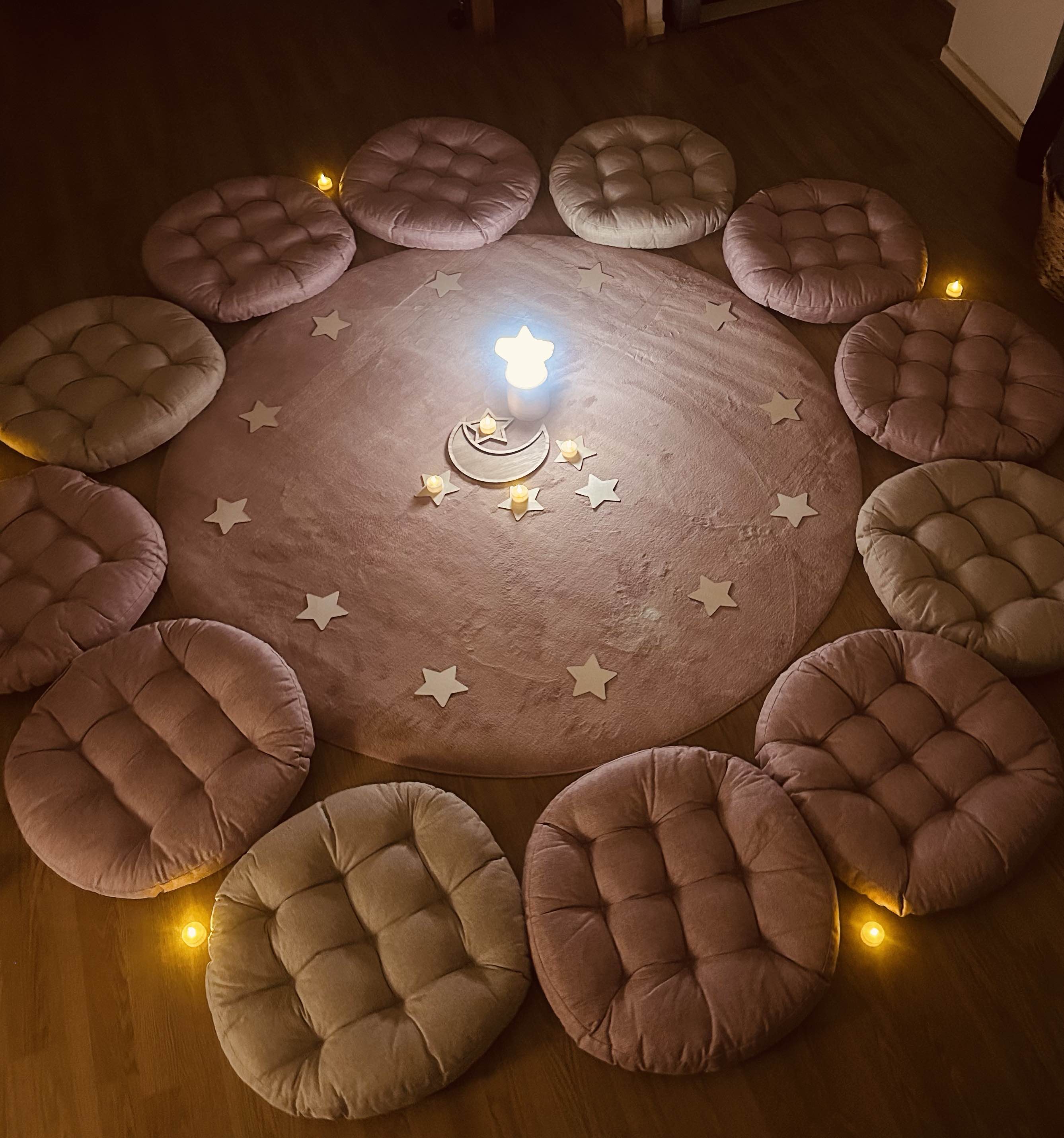 Tapis rond entouré de coussins disposés en cercle, bougies et étoiles en bois au centre, pour l'atelier du soir